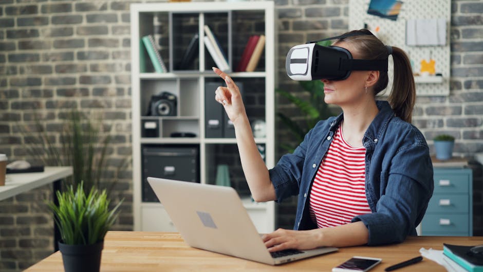 A woman using a VR headset while working on a laptop, exploring virtual reality in a modern office setting.